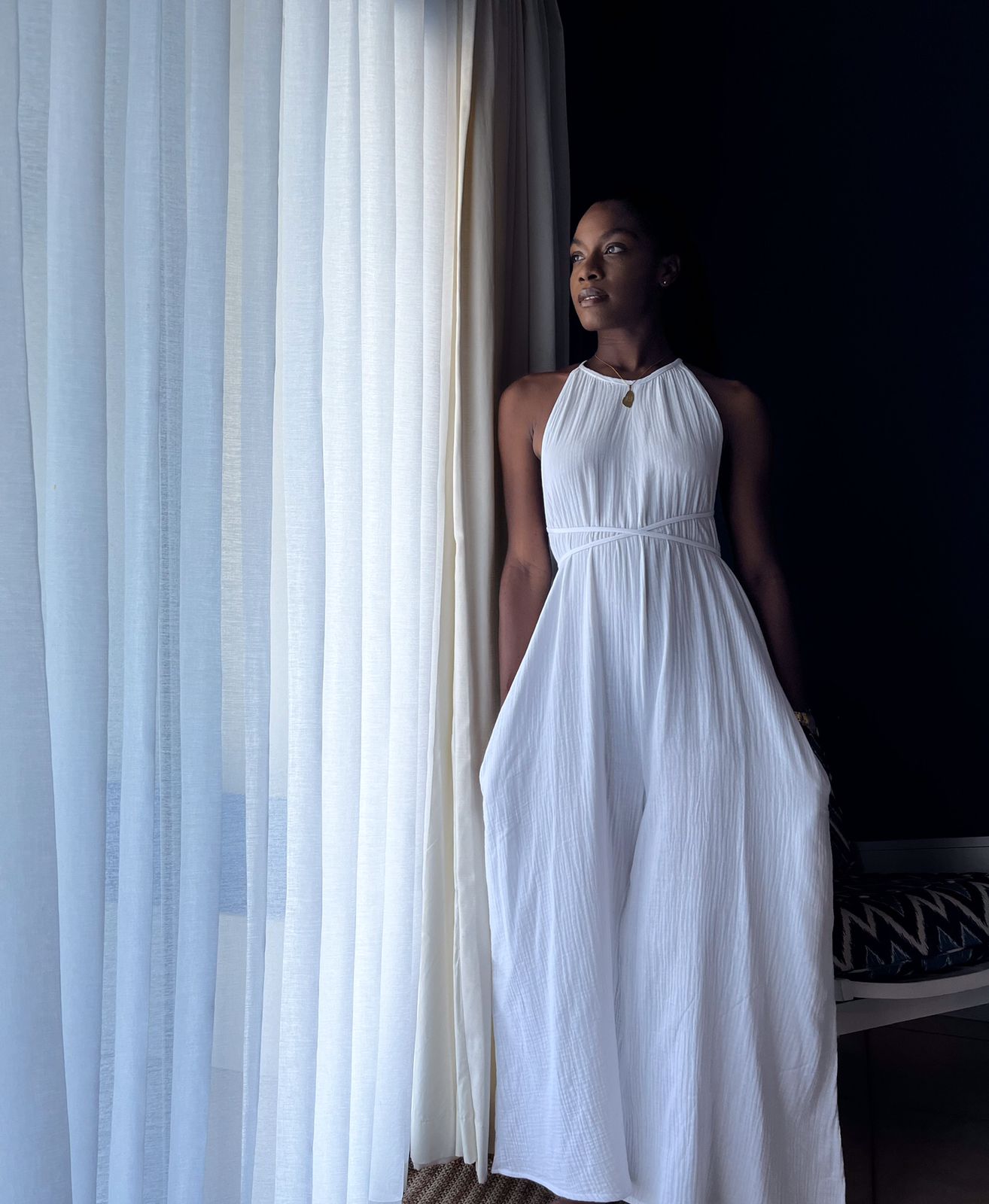 Model, Shadyn, wearing the Ocean Whisper jumpsuit standing by sheer curtains